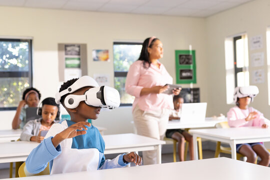 African American male child reaching forward wearing white VR headset and blue shirt in classroom