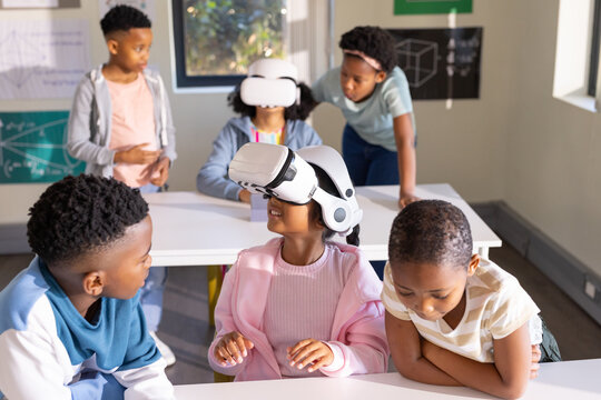 African American students wearing white VR headsets and interacting at classroom desks with posters