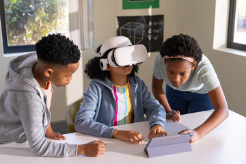 African American students collaborating at lab table, female wearing white VR headset using tablet