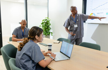 African American team meeting at clinic, standing male presenting, pointing at display, copy space