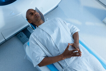 Male patient lying supine in gantry on table with head support in radiology suite, wearing gown