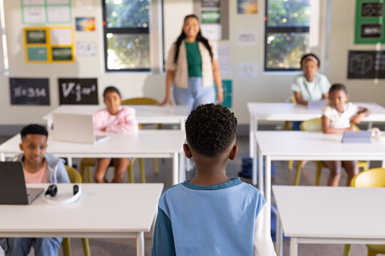 African American teacher leading lesson with students in classroom with white desks and laptops