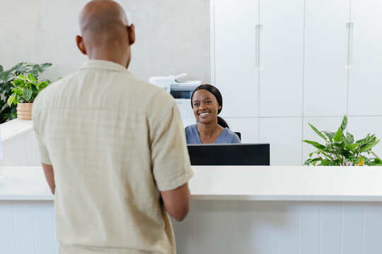 African American receptionist sitting at desk in blue top, male visitor standing near printer