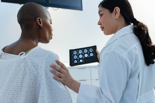 Diverse female doctor  and  patient holding tablet showing brain scans, touching her shoulder in cli