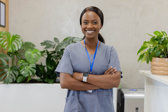 African American woman standing at clinic reception wearing gray scrubs, lanyard and smartwatch