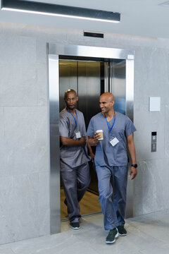 African American men walking out metal lift wearing blue scrubs with ID badges, one holding coffee