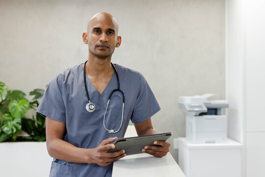 African American male standing at clinic reception holding tablet with stethoscope in gray scrubs