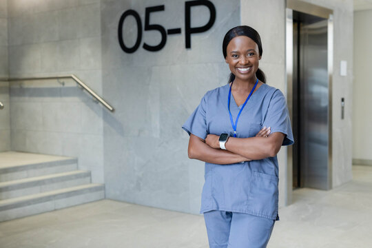 Female nurse smiling near elevator, 05-P signage in lobby, blue scrubs, ID badge, copy space