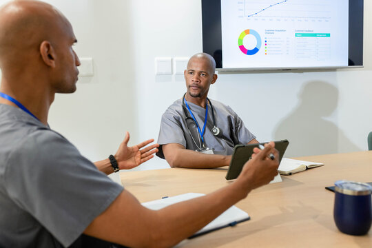 African American male colleagues in scrubs discussing charts on tablet with stethoscope in clinic
