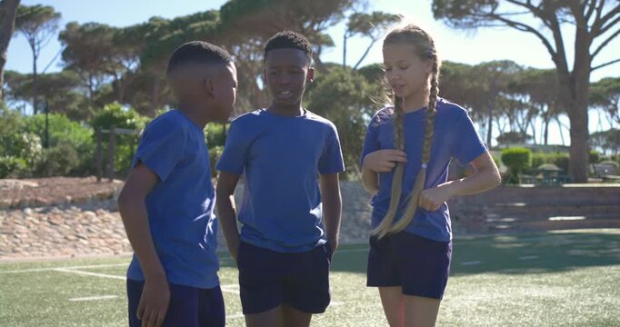 Diverse teens after brief talk placing hands in stack on synthetic turf, celebrating in blue shirts