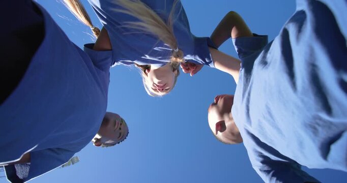 Diverse youths in blue shirts huddling, braided girl adjusting shirt starting hand stack pregame