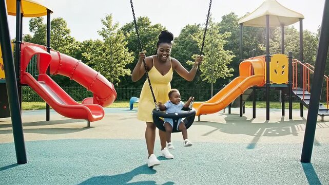 Joyful mother pushes her baby on a swing set at a vibrant outdoor playground capturing a heartwarming moment of family fun and childhood happiness