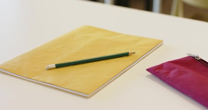 Camera is zooming and focusing, keeping yellow notebook with green pencil still on desk for display