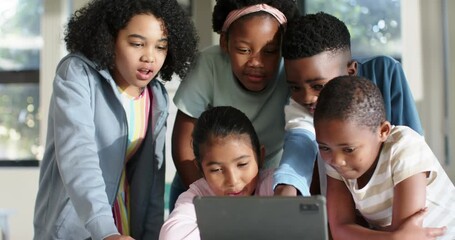 Diverse preteen children leaning over tablet on low table in classroom, reacting to surprising clip - Powered by Adobe