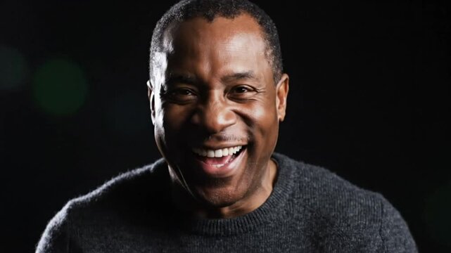 Cheerful African American man laughs heartily while looking at the camera against a black background