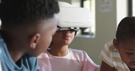 African American children watching girl lowering white VR headset after placing it to start class