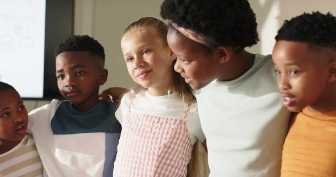Diverse children linking arms with girl speaking, shifting and laughing by screen at school