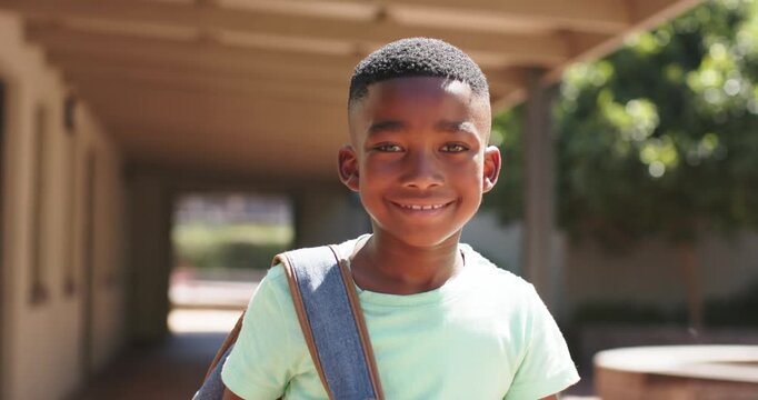 African American child walking from corridor, smiling and holding backpack, wearing light green tee