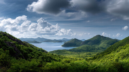 Breathtaking Scenic View of Lush Green Mountains Meeting Calm Ocean Under Dramatic Sky with Fluffy Clouds