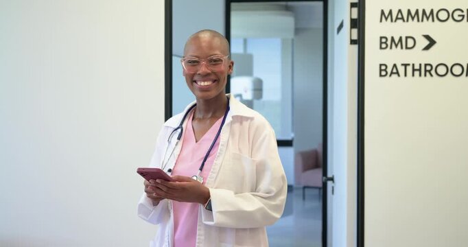 Adult African nurse in scrubs with stethoscope walking through clinic reading phone message smiling