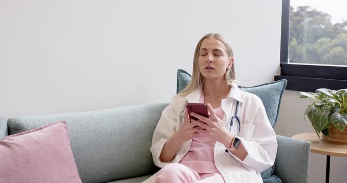Woman in scrubs with stethoscope holding phone, resting, placing on couch in staff room, copy space