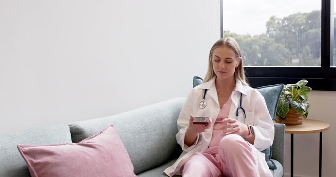 Female nurse in scrubs with stethoscope scrolling phone after message, rising to window, copy space