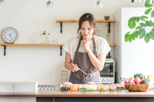 A young Asian woman cooking in the kitchen (worried, confused, thinking, choosing)