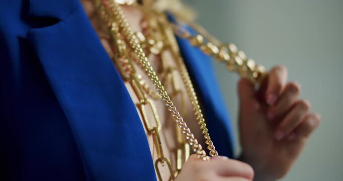 Woman in a blue jacket wearing and adjusting many layers of gold necklaces as a luxury fashion statement
