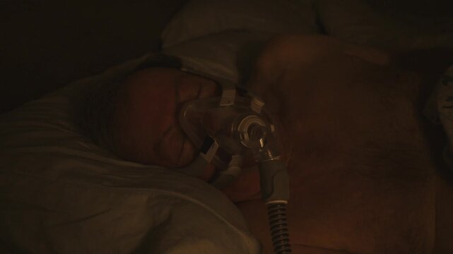 slow nighttime bed view close-up of senior citizen male with CPAP mask resting peacefully on his side at night