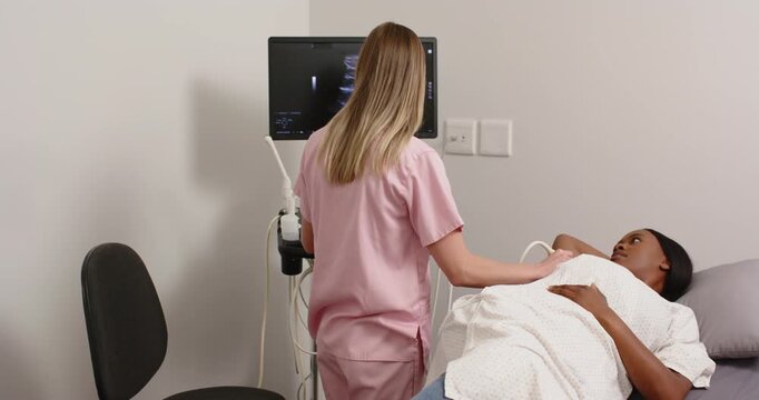 Female sono tech pink scrubs with African American patient during exam, scanning abdomen with probe