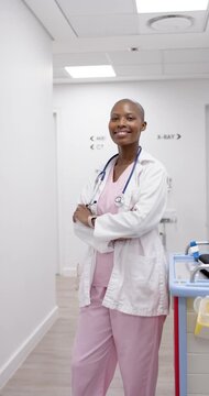 Vertical video: Woman clinician in coat standing arms crossed in corridor, camera moving reassuring