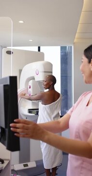 Vertical video: Diverse patient and tech preparing mammogram, tech tapping console aligning breast