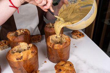 A confectioner filling several panettones with pistachio cream.