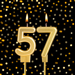 Number 57 birthday candle on a black background with blurred lights
