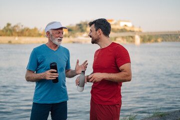 Obraz premium Senior and young man talking after exercising by the river