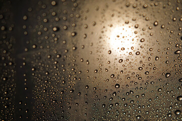 Water droplets on glass surface with warm backlit glow and bokeh effect.