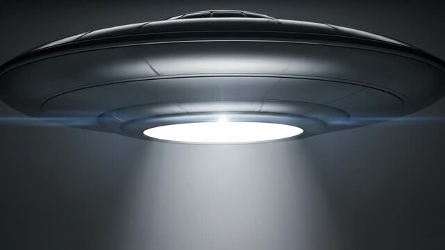 Sleek llic UFO hovers in the dark, emitting a bright beam of light.