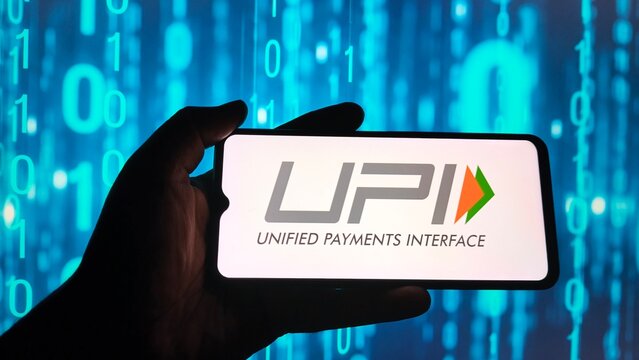 Hand holding smartphone displaying upi unified payments interface logo against a blue digital background with binary code