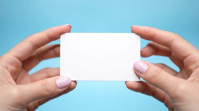 Close up on female hands holding a blank white business card against a blue background