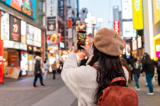 Young female tourist taking a photo of tourist and nightlife areas in Dotonbori district in Osaka, Japan