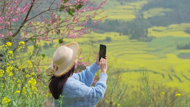 Young woman tourist enjoying and taking a photo the beautiful canola fields while traveling in Luoping, China