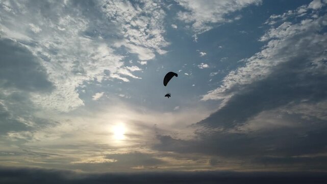 sunset sky paraglider silhouette over sea, drifting through dramatic cloudscape near glowing sun on