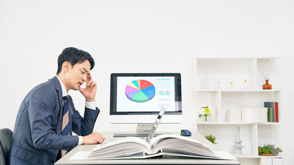 オフィスで仕事をしながら悩む男性ビジネスパーソン