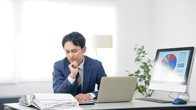 オフィスで仕事をしながら悩む男性ビジネスパーソン