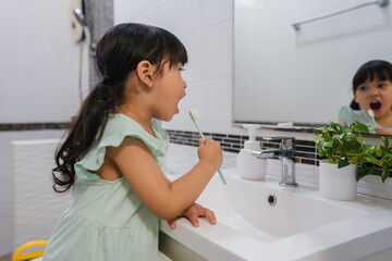 girl child brushing teeth at reflection in mirror in bathroom