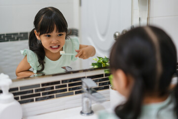 girl child brushing teeth at reflection in mirror in bathroom