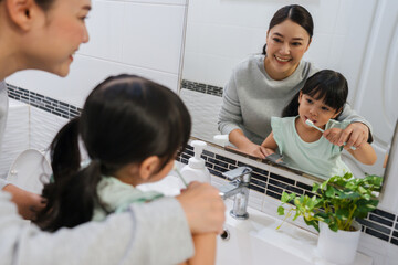 mother teaching girl child to brushing teeth at reflection in mirror in bathroom