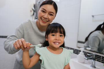 mother teaching girl child to brushing teeth in bathroom