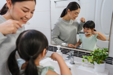 mother teaching girl child to brushing teeth at reflection in mirror in bathroom