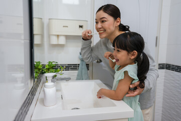mother teaching girl child to brushing teeth and tongue at reflection in mirror in bathroom